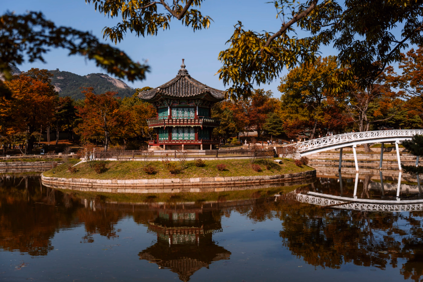 A bridge connects a small island where a pagoda stands reflected in the water that surrounds it on all sides