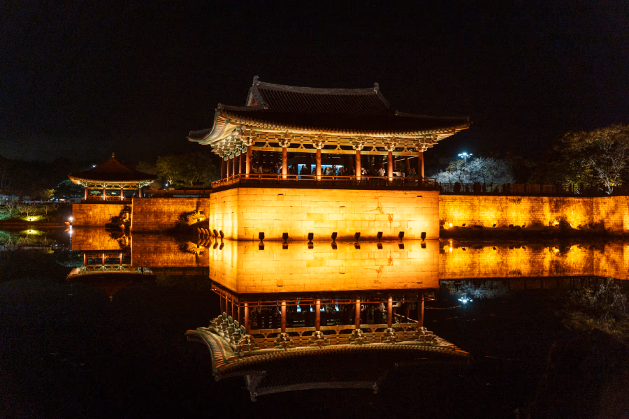 Powerful lights illuminate a row of temples at night, creating an excellent reflection in the water below at  Donggung Palace