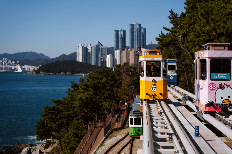 Colorful sky capsule ride along rails with the sea to the side and the glass towers of Busan in the background