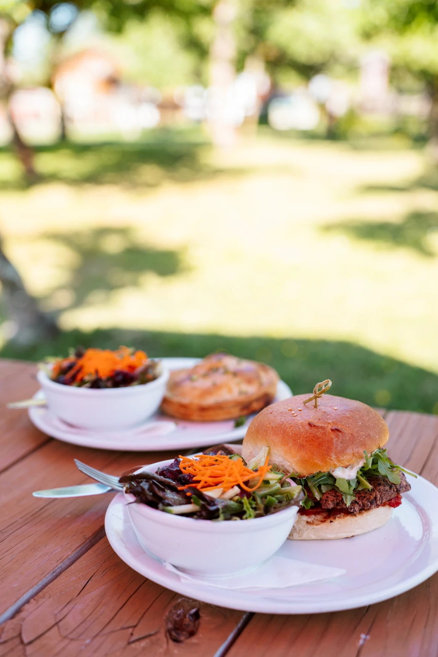 Two veggie burgers and two bowls of salad served in white dishes on a red picnic table