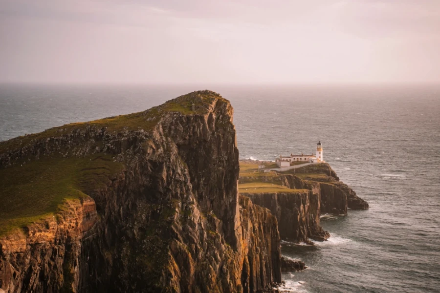 A white lighthouse stands at the end of a rugged stretch of headlands