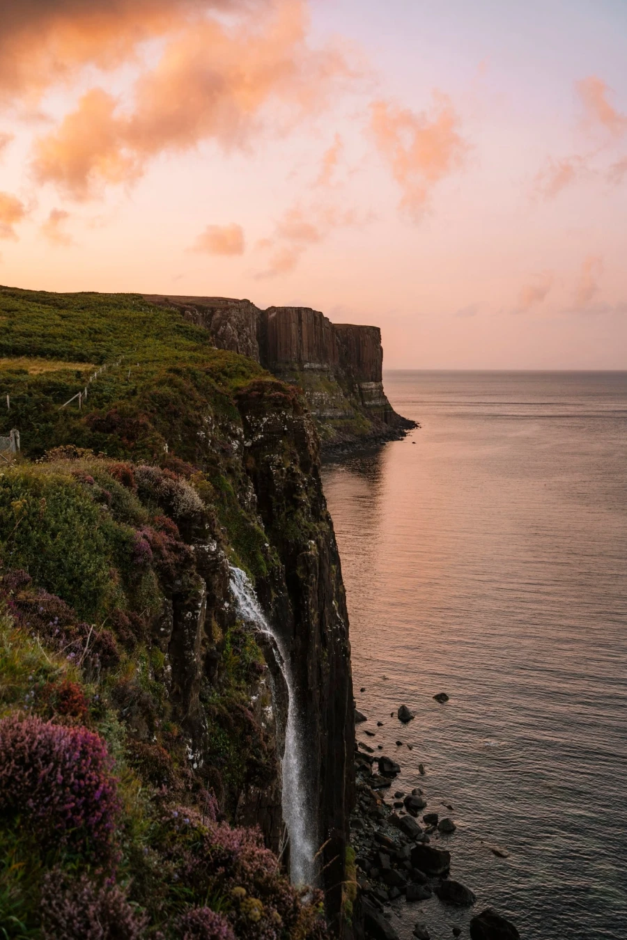 Water pours over a sheer cliff into the sea below while the sky glows in the sunset light
