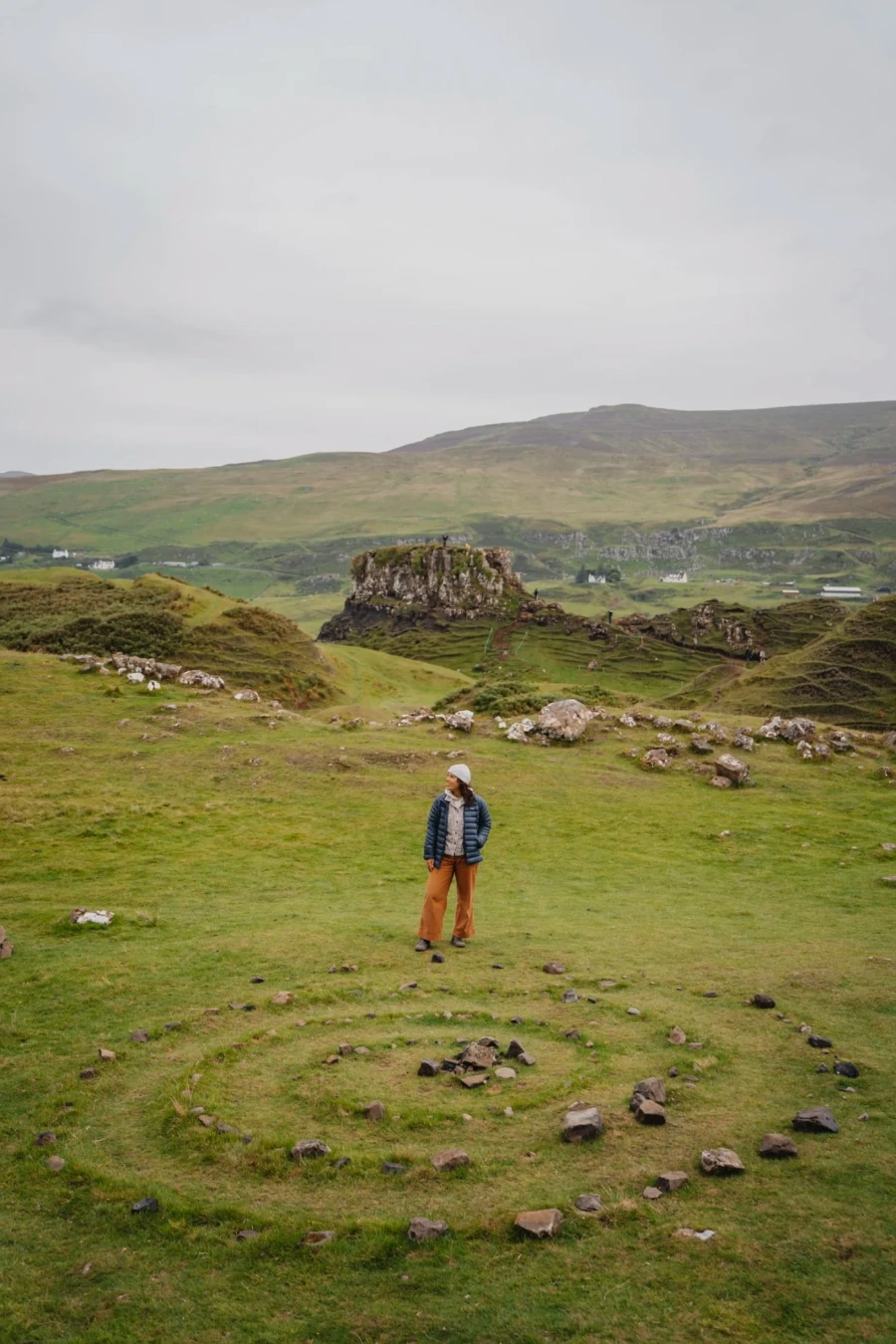 A woman standing in front of a whimsical stone spiral set in the grass at Fairy Glen
