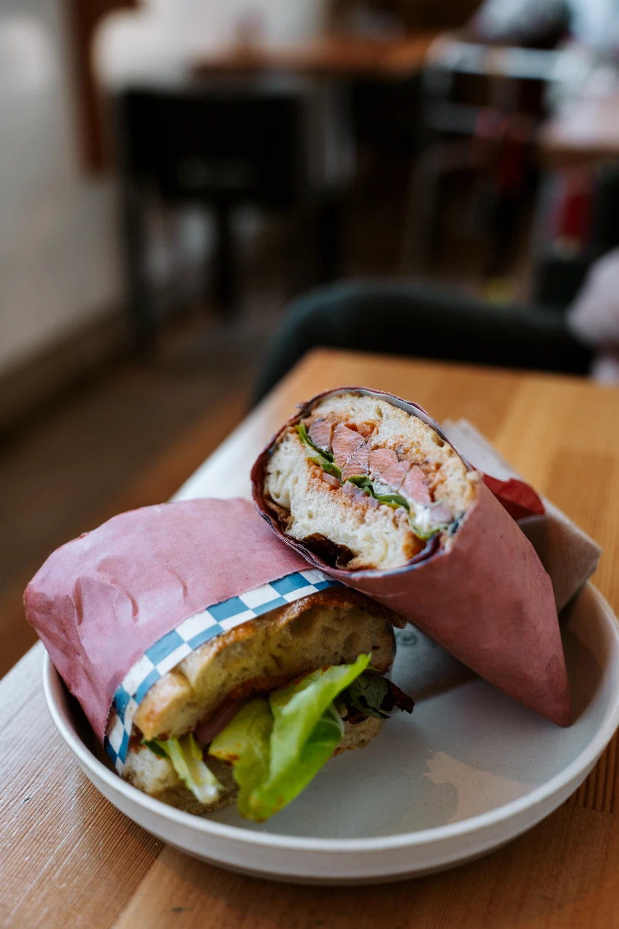 A sandwhich wrapped in paper is sliced in half and presented in an appetizing way