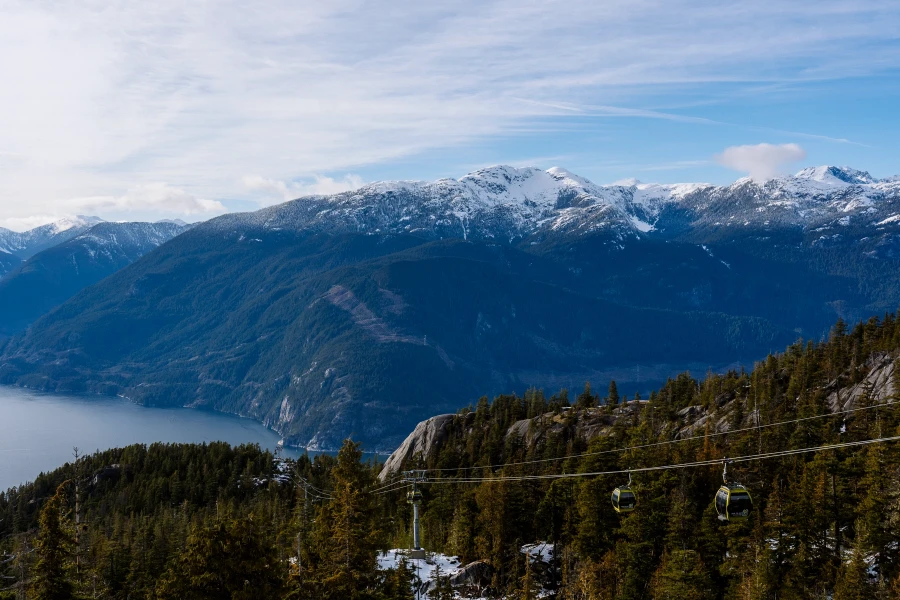 Gondolas coming up and down a forested mountainside with distant snowy peaks visible in the distance in Squamish, BC