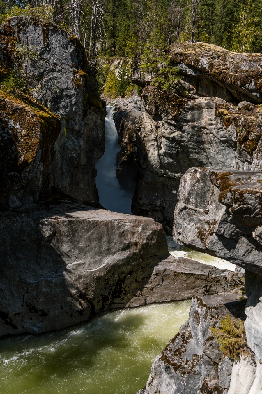 A powerful surge of water pours through a small channel between rocks