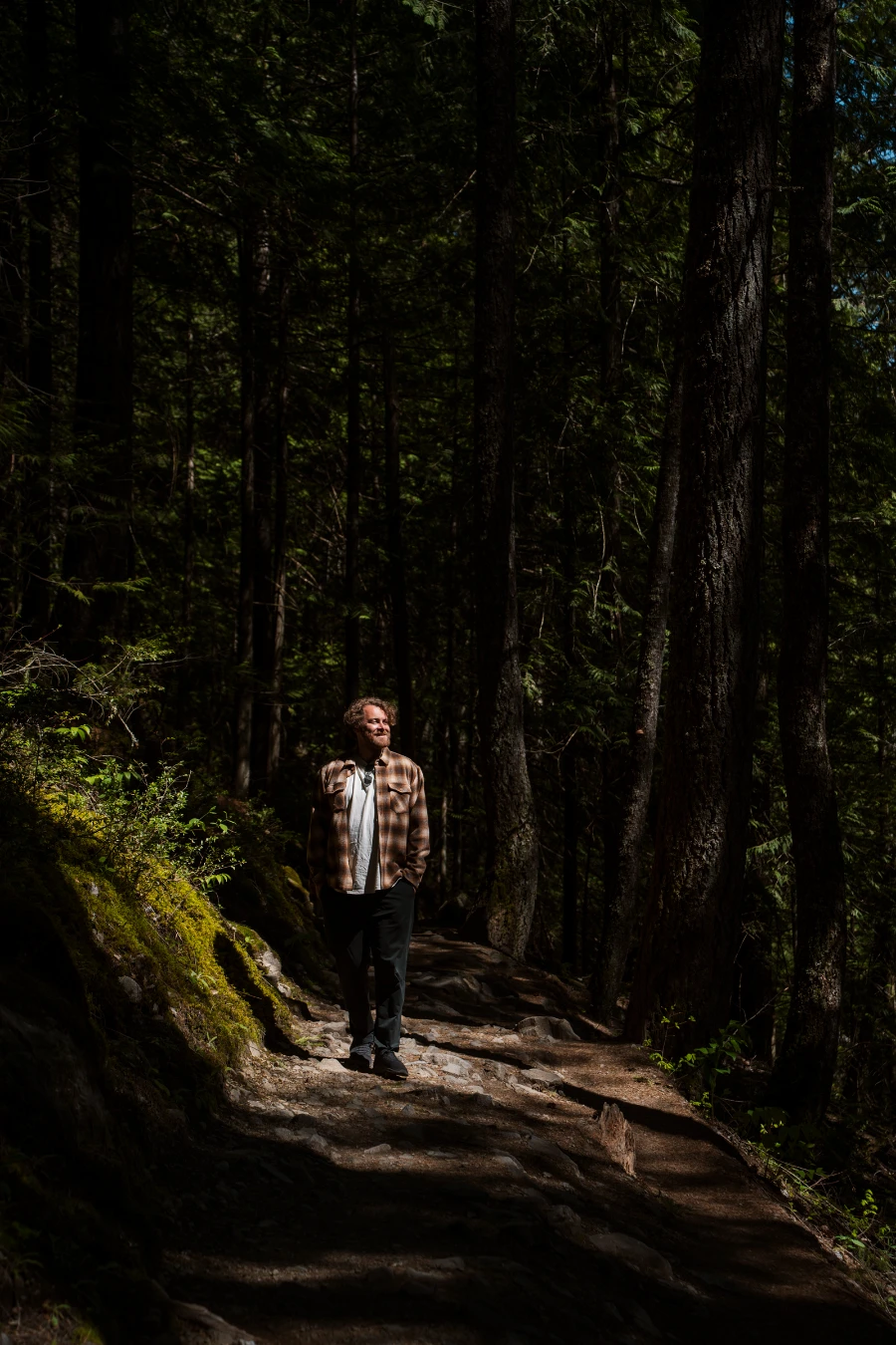 A man walking down a dirt path through a spot of sunlight while surrounded by trees
