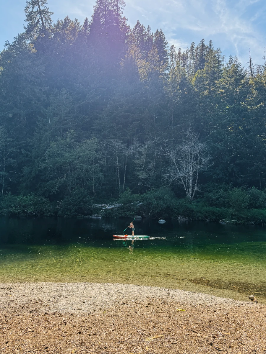 A child paddles a paddleboard across a calm, turquoise river in Sooke Potholes Provincial Park