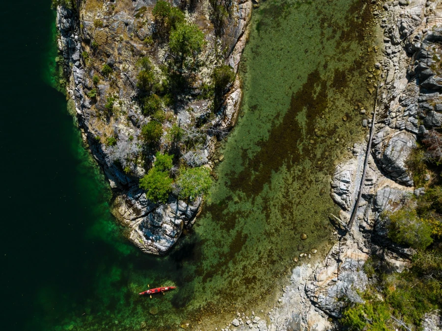 Stony shores create a U shaped bend in the shallow water and a red kayak navigates the turn