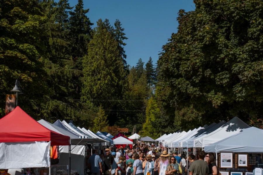 Two rows of tents run along a tree-lined road while a dense crowd walks between them