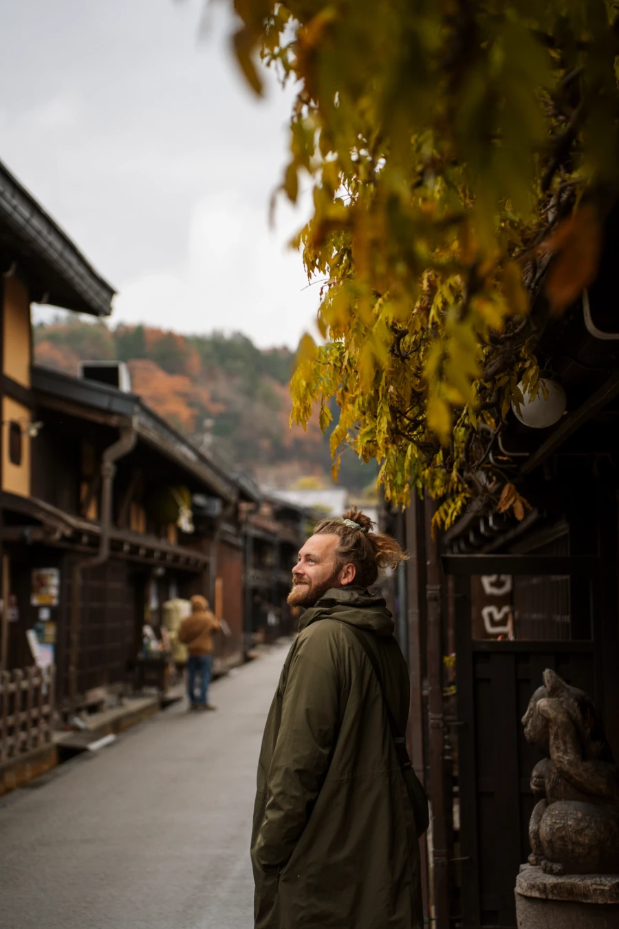 A man leaning on a wooden storefront looking down an empty street in Takayama, Japan