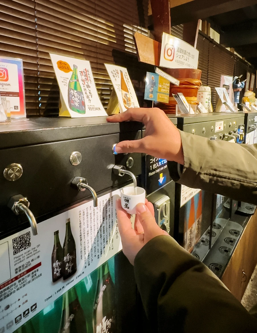 Two hands handle a Sake dispensation machine  in Takayama, Japan