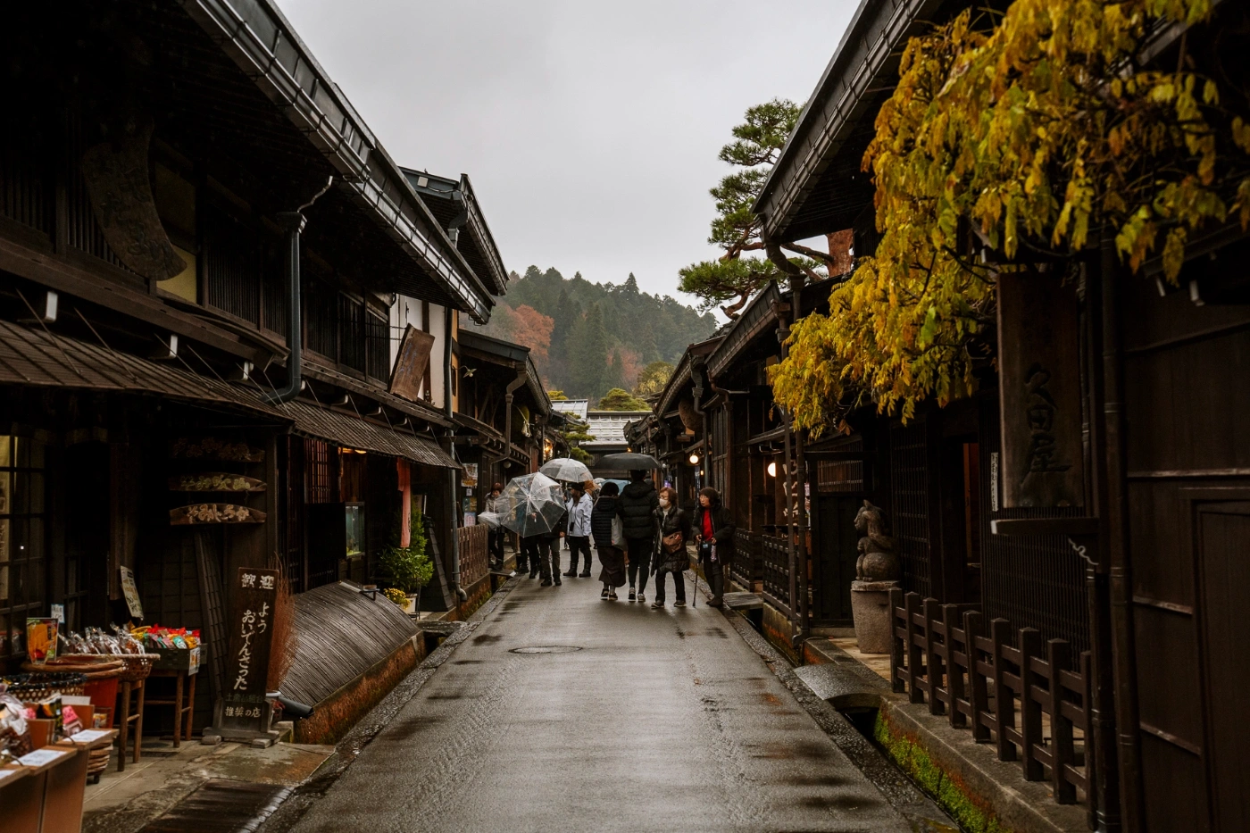 A crowd of tourists walk down a rainy street flanked by wooden storefronts 