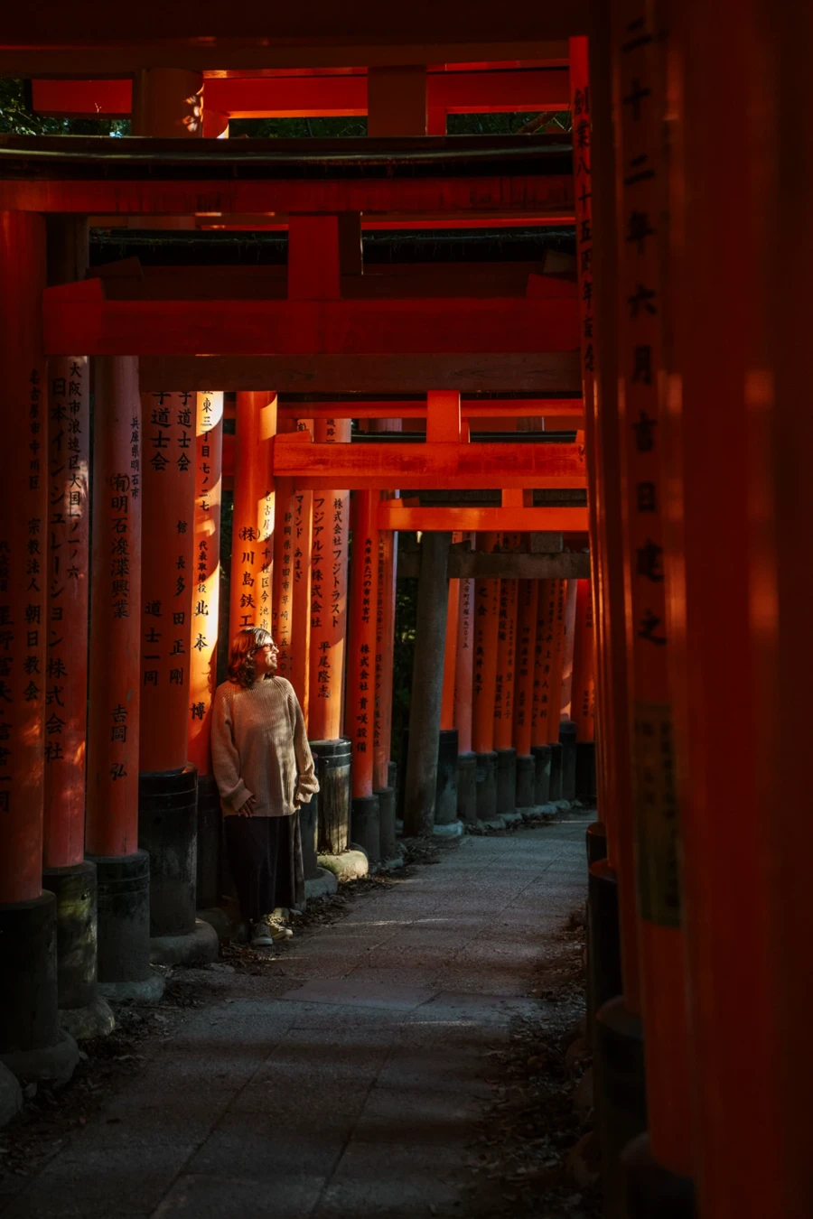 A woman stands inside a row of red tori gates leading to Fushimi Inari Taisha, Kyoto, Japan