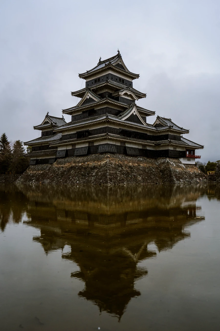 A large castle built on a bed of stones and surrounded by a massive moat is reflected well in the calm water below