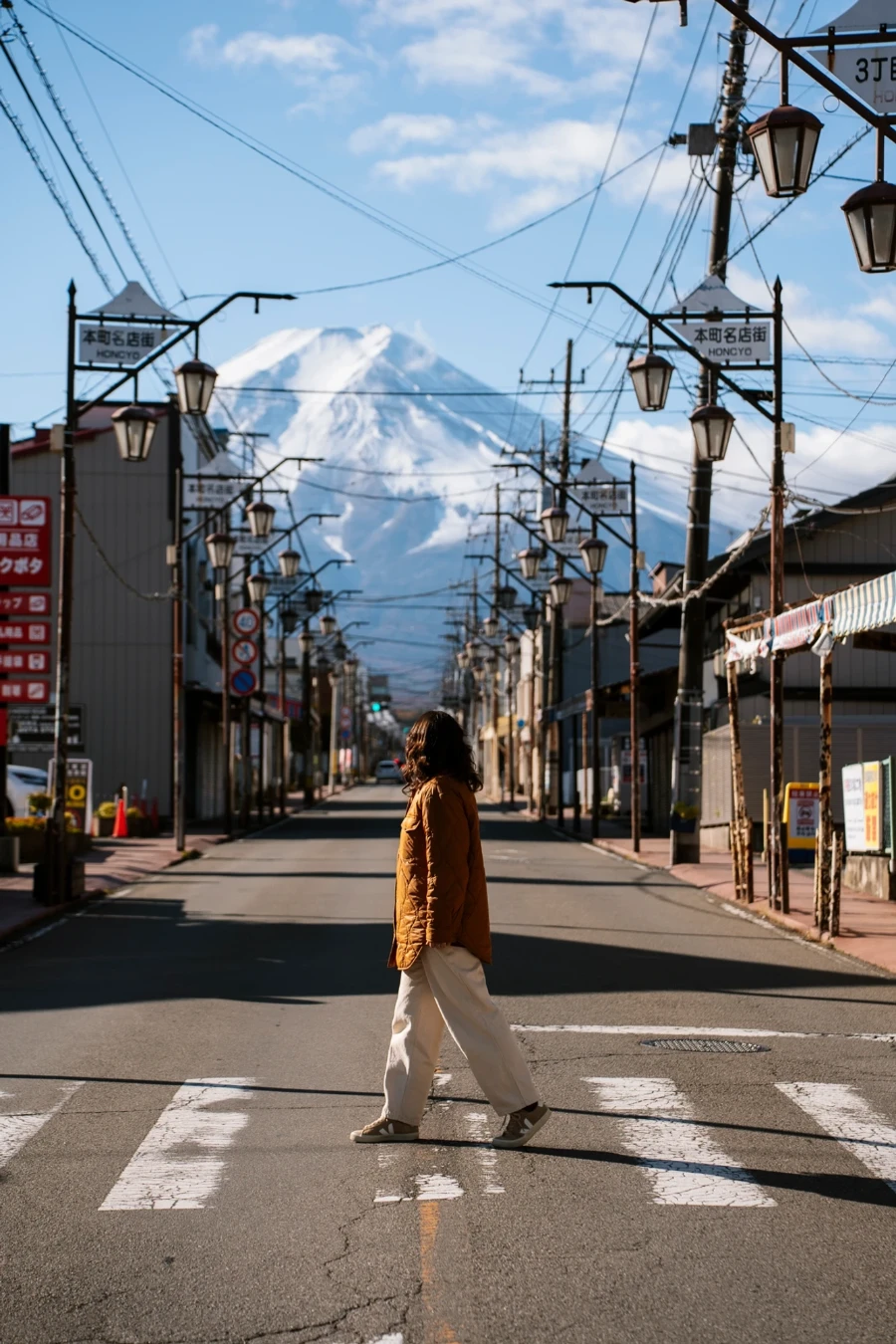 A woman walks across a cross-walk with Mt. fuji framed at the end of the street