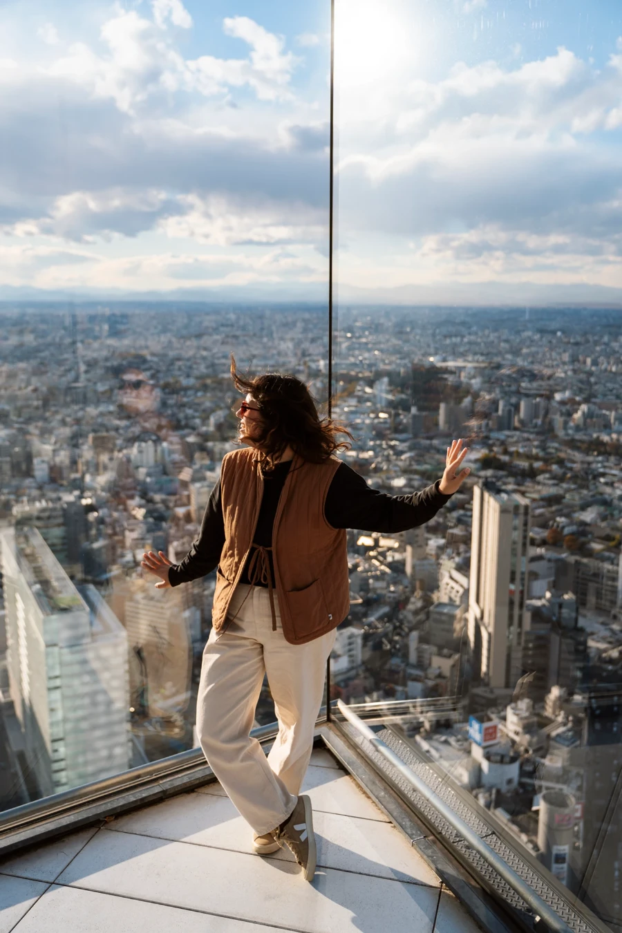 A woman stands leaning on a glass wall high above the cityscape of Tokyo Japan