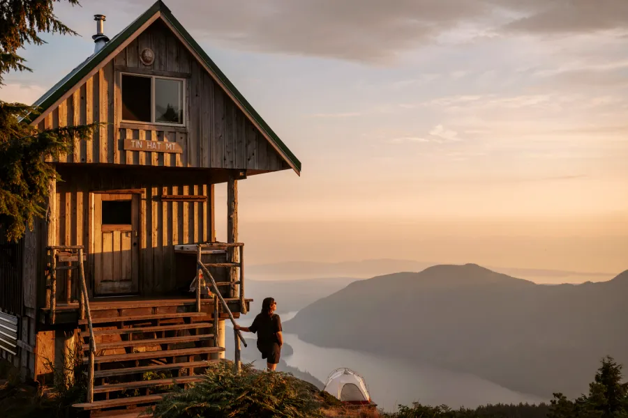 Woman stands next to a cabin with a sign labeling it Tin Hat Hut