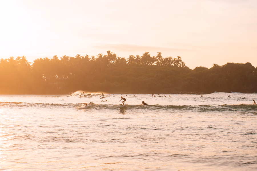 Several surfers riding 2 separate long waves in the sunset light at Hiriketiya Beach