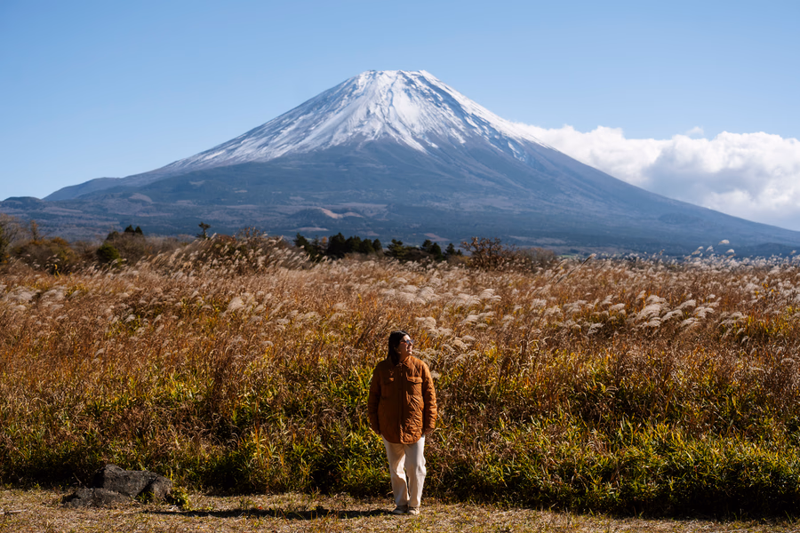 A woman stands in front of an open field with Mt. Fuji on the horizon, Japan