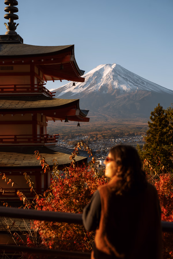 A woman stands in front of a five story pagoda that is framing the snow capped peak of Mt. Fuji
