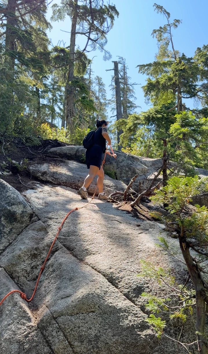 A woman climbs up a steep stretch of exposed granite using a rope to help her climb