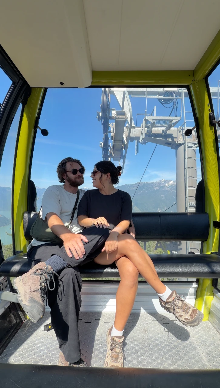 A man and a woman sitting arm in arm in a green gondola car riding up the Sea to Sky Gondola