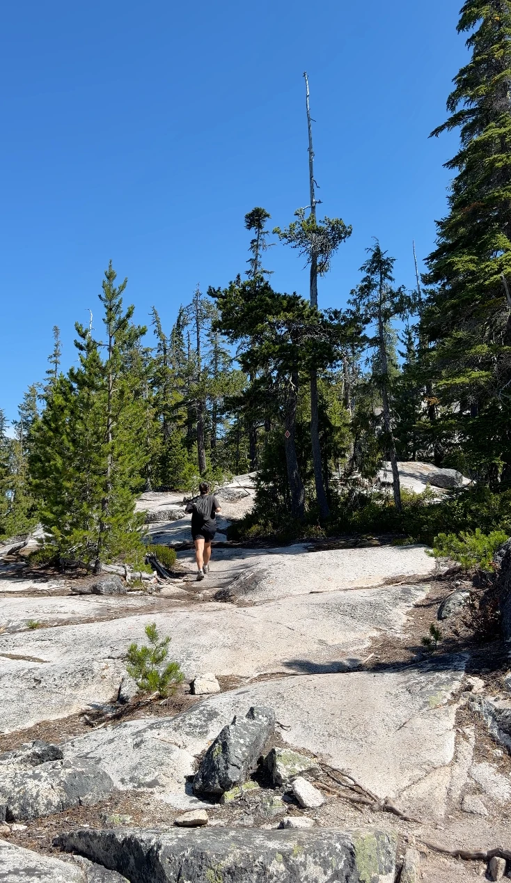 A woman walks along a stretch of bare exposed granite slabs along a ridgeline of the Al’s Habrich trail