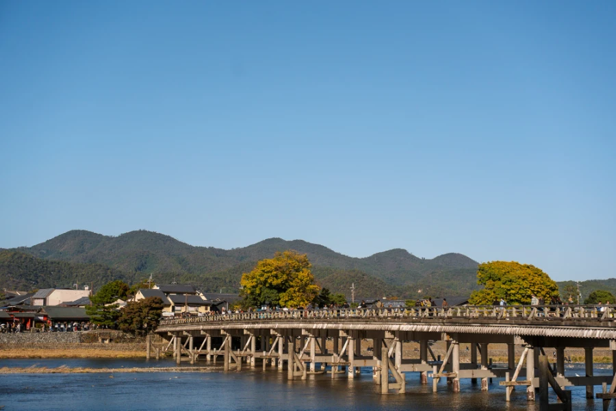 A large wooden bridge crosses a shallow river in Arashiyama Japan