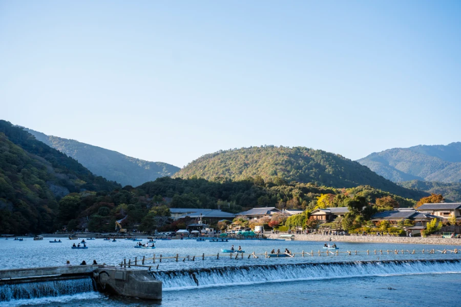 Forested mountains cast a shadow on several boats floating on Hozugawa River
