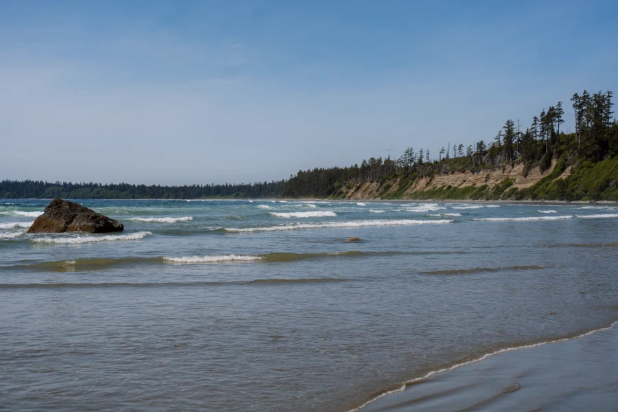 Gentle waves roll over shallow waters onto the sandy shore of Florencia Bay at high tide with huge sand stone cliffs bordering the beach in the distance