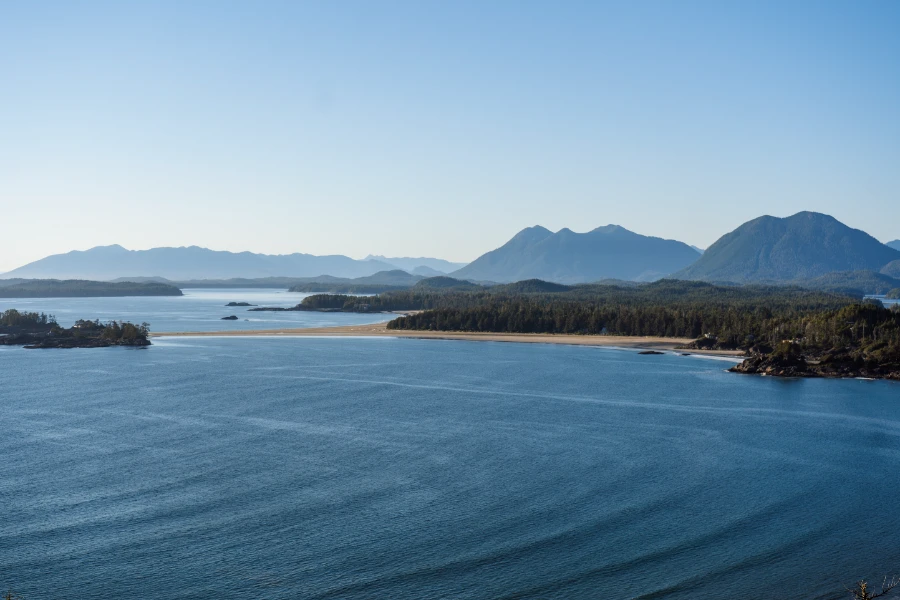 Dozens of rows of waves radiate into a large sandy bay with cone shaped tree-covered mountains on the horizon at Chesterman Beach in Tofino