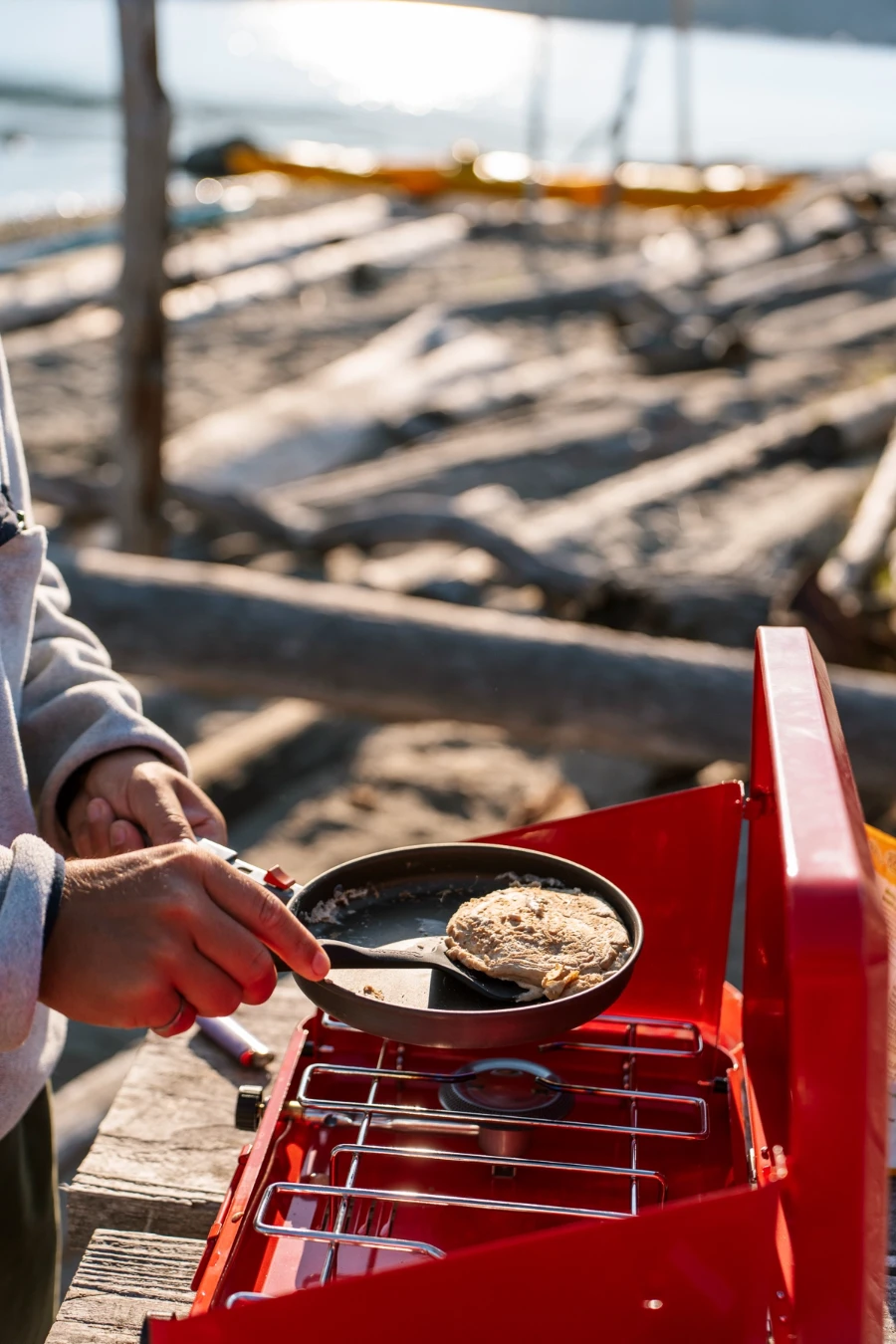 man flipping a pancake on a red camp stove while cooking breakfast on a beach on Thormanby Island, BC