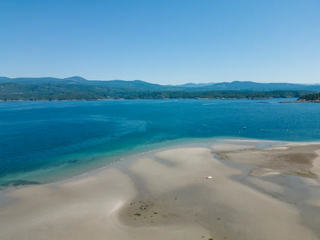 wide stretch of white sand at low tide along Vaucroft beach on Thormanby Island with the Sunshine Coast on The Horizon