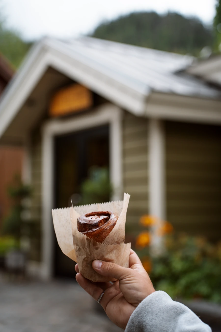 A hand holds a cinnamon roll up in the air in front of BReD bakery in Whistler Creekside