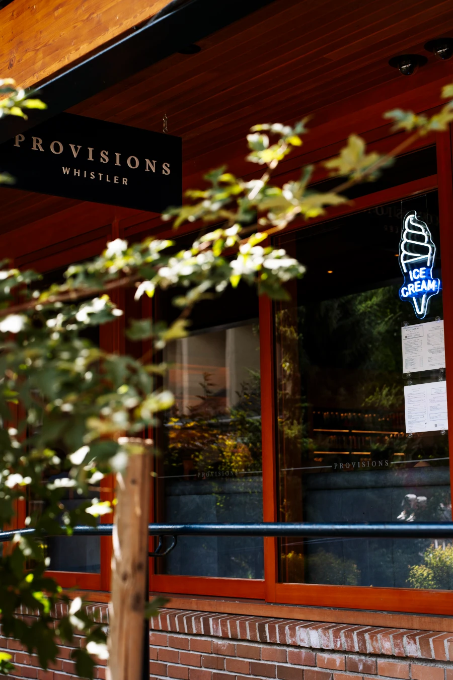 A lit neon sign shaped like an ice cream cone reads ‘Ice Cream’ in the window of Provisions coffee shop in Whistler Village
