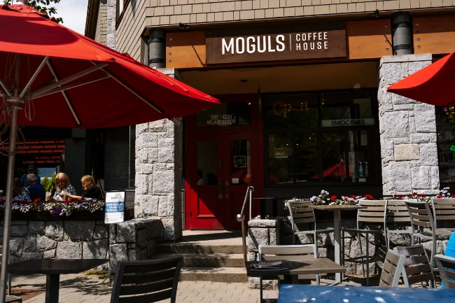 Several empty chairs set beside tables outside the stone facade of Moguls Coffee House