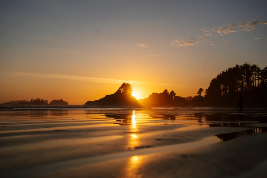 Golden light of the setting sun reflected on the wet sands of Cox Bay as the sun dips behind pettinger point in the distance