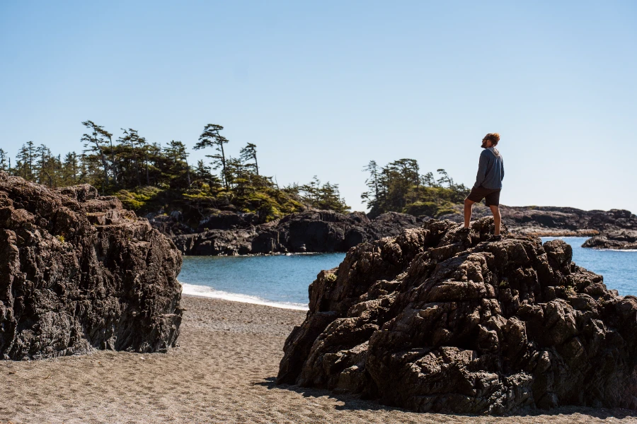 A man stands atop a large rock on the sandy shores of South Beach near Tofino