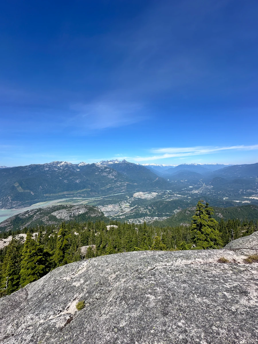 A bare stone cliff in the foreground with an expansive view of the Squamish Valley and the surrounding mountains