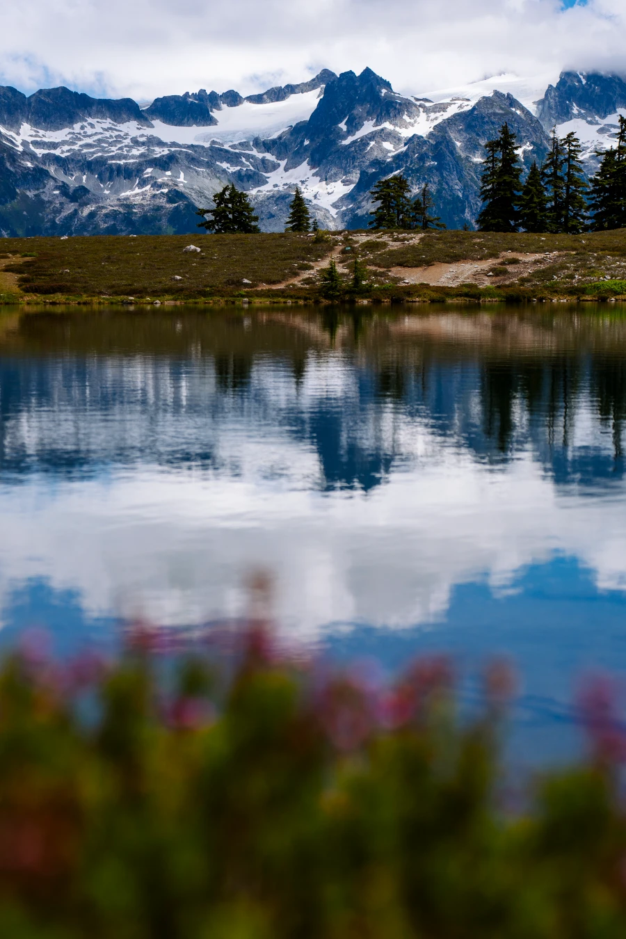 A line of jagged peaks with glaciers between them reflected in a still alpine lake