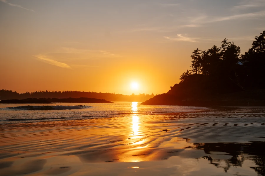 The warm light of the setting sun is reflected in the wet sand at tin wis beach during low tide in Tofino