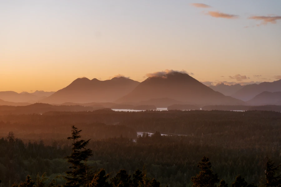 Misty cone shaped mountains in the distance glow in a pink afterglow of the sunset from Radar Hill in Tofino