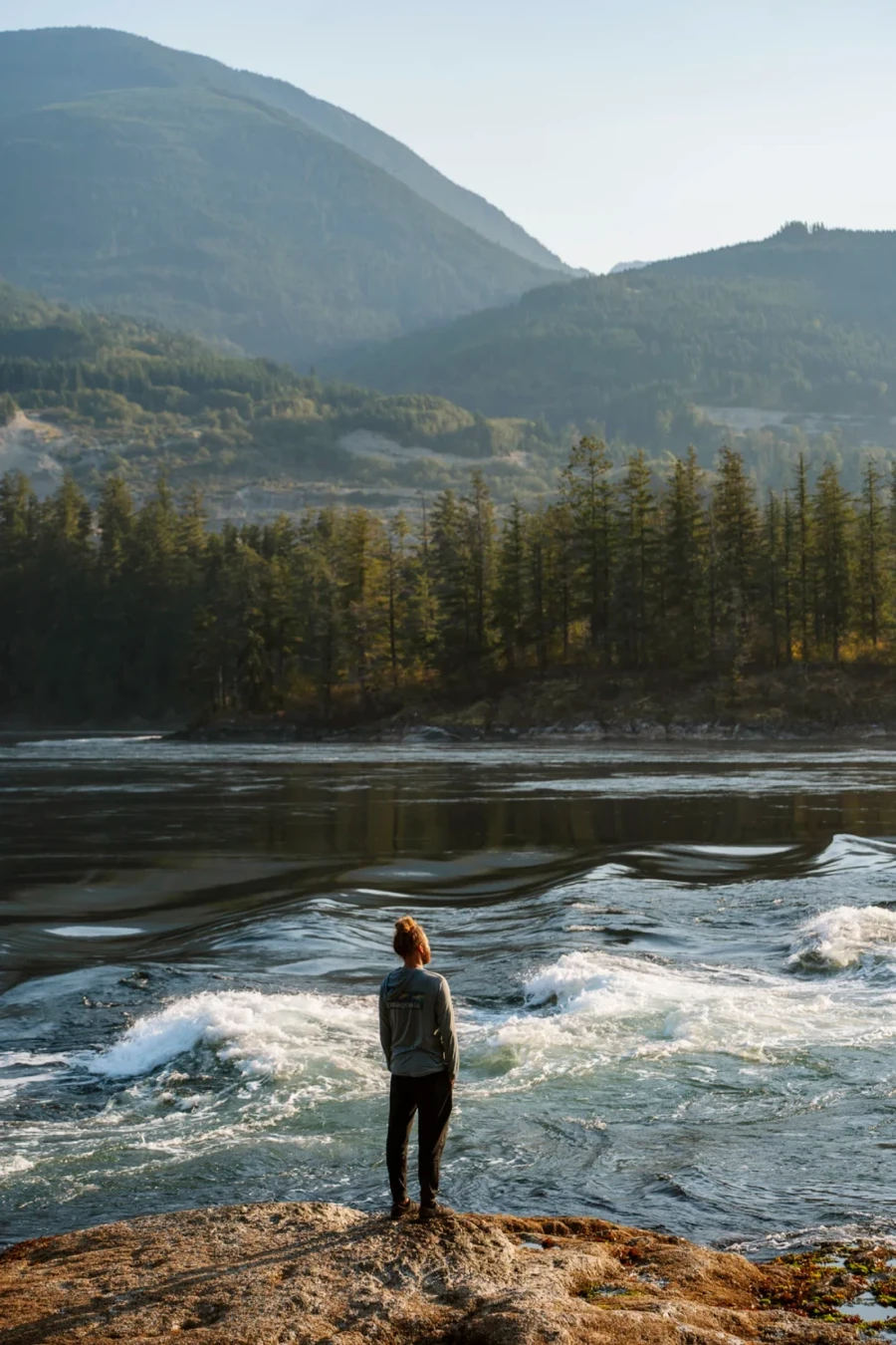Man standing with hands in pockets looking at a heavy flowing Skookumchuck Rapids