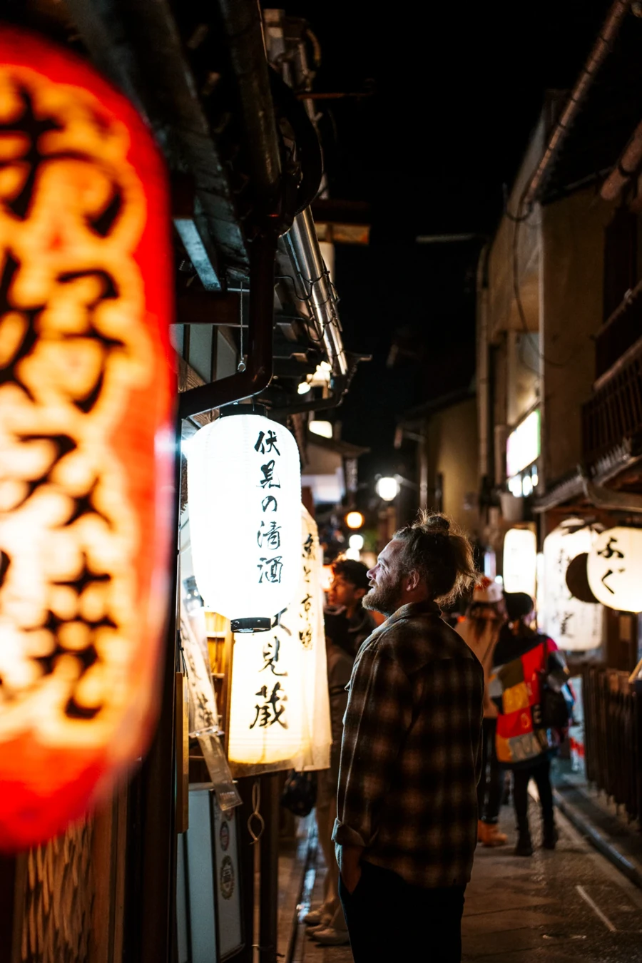 A man looks into a storefront along a lantern lit street busy with night time crowds