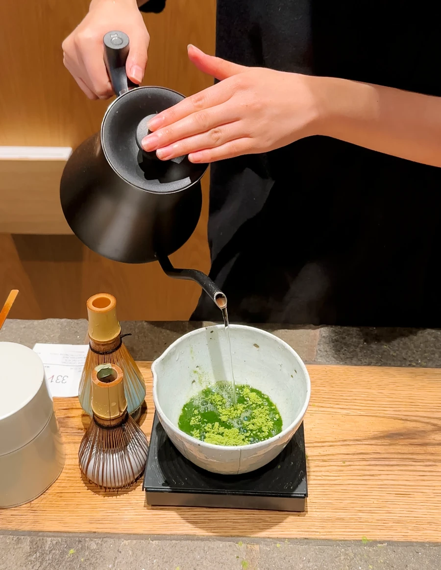 Two hands poor water from a black kettle into a bowl of matcha powder at Gokago Matcha, Kyoto