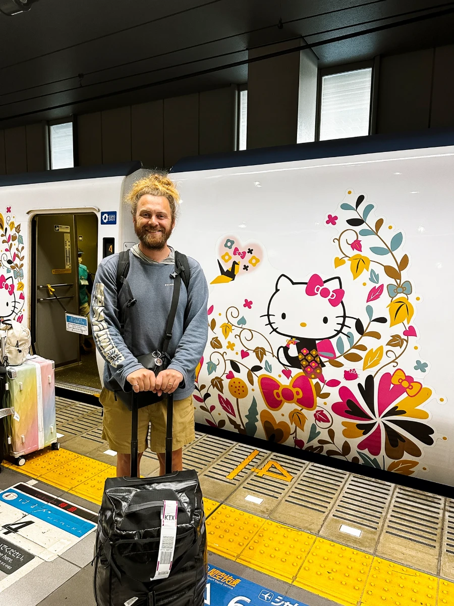 A man with a suitcase standing in front of a Hello Kitty Themed Train, Osaka, Japan