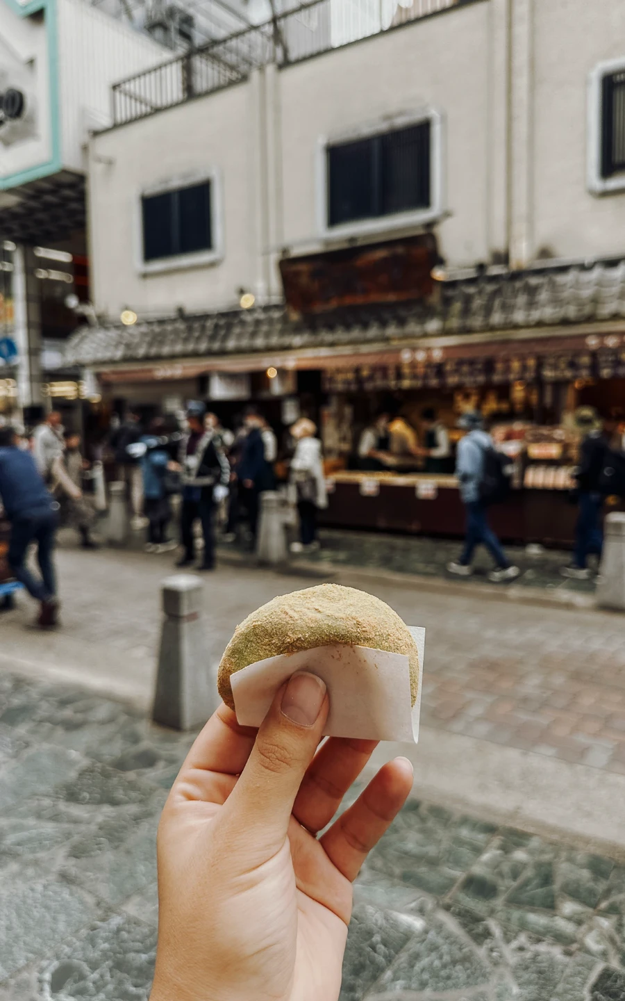 A hand holds a fresh Mochi up with the Mochi shop behind it at Nakatanidou Nara Park, Japan