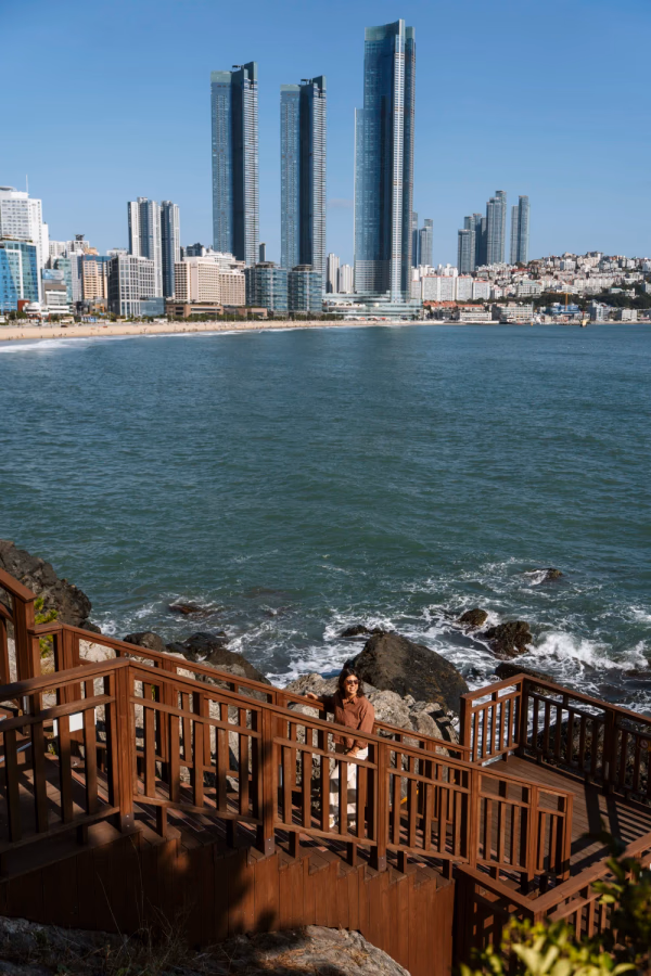 A woman walks up a wooden staircase near the sea along a white sand beach in Busan, South Korea