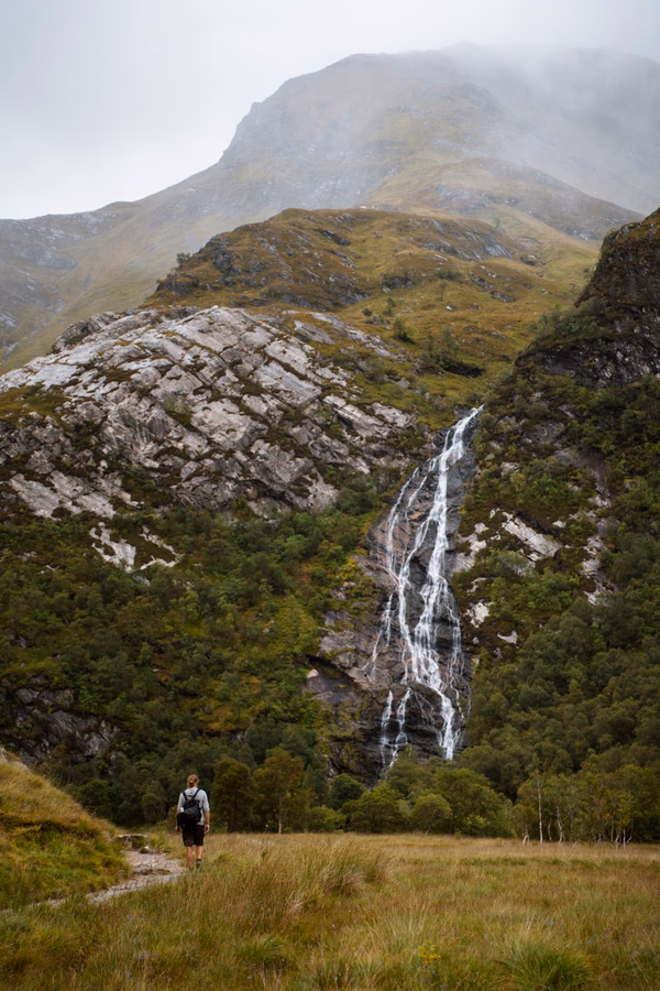 A man walks down a gravel path towards Steall Falls which is visible in the distance